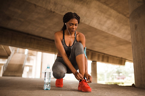 Giovane donna afroamericana legare le scarpe da ginnastica prima di iniziare a correre
 - Foto, immagini