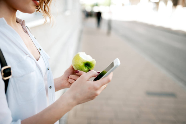 Woman using smartphone and eating apple in city. Close up. - Photo, image