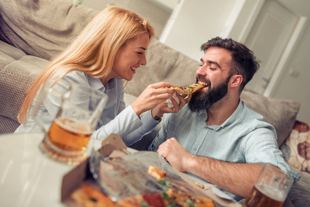 Ζευγάρι έχοντας το γεύμα στο σπίτι, τρώγοντας πίτσα. Άνθρωποι, αγάπη, φαγητό και τρόπο ζωής έννοια. - Φωτογραφία, εικόνα