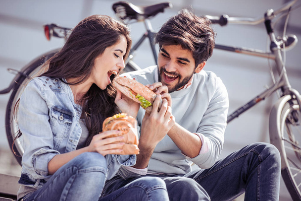 Couple having breakfast outdoors,they are sharing a sandwich. - Foto, imagen