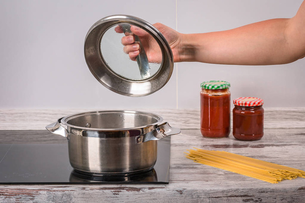 Cook a tésztát, forró serpenyőben, fazék, tűzhely, konyha, pan, kéz, a fekete nyomólapra fém serpenyőben fedő - Fotó, kép