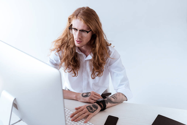high angle view of stylish tattooed businessman with curly hair looking at computer in office - 写真・画像