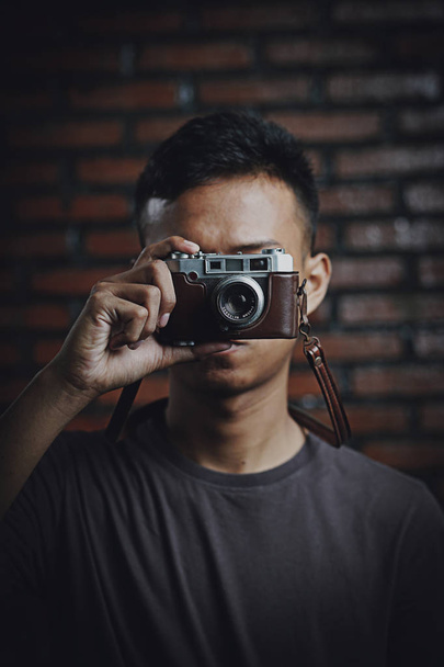 Aasialainen mies ottaa kuvan Vintage-kameralla tiiliseinällä Backg
 - Valokuva, kuva