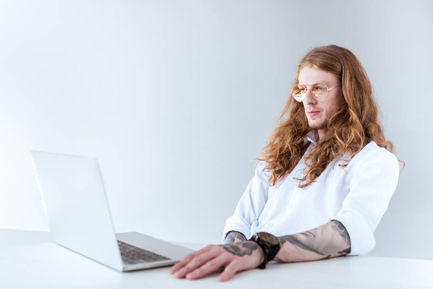 side view of stylish tattooed businessman with curly hair looking at laptop - Photo, Image