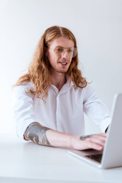 hombre de negocios tatuado elegante con el pelo rizado que trabaja con el ordenador portátil en la oficina
 - Foto, Imagen