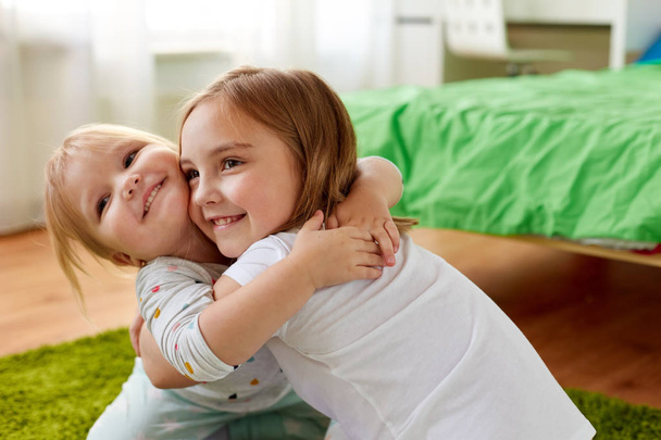 happy little girls or sisters hugging at home - Fotografie, Obrázek
