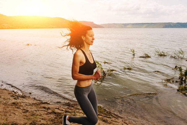 eine schöne sportliche Frau, die am Ufer eines Sees beim Sport rennt - Foto, Bild