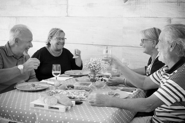 домашня сцена для групи старших в чорно-білому кольорі. Їжа та сміх разом з чашками вина та їжі. приємний час з людьми і смачні речі на столі
 - Фото, зображення