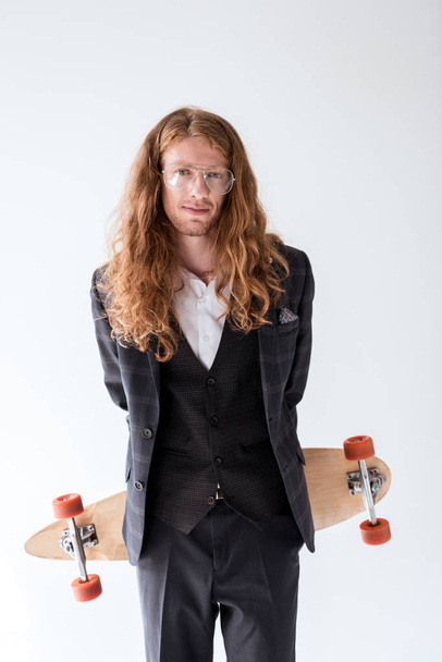 stylish businessman with curly hair holding longboard above back isolated on white - Foto, afbeelding