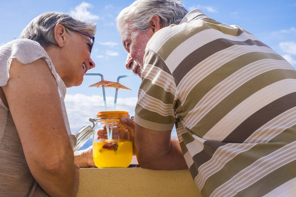 άνδρας και γυναίκα ενήλικες ηλικίας 60 ετών πόσιμο υγιή φρούτα χυμός από vase γυαλιού υπαίθρια στη βεράντα. ωραία θέα και όμορφοι άνθρωποι. - Φωτογραφία, εικόνα
