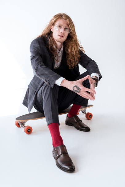 stylish businessman with curly hair sitting on skateboard - Foto, afbeelding