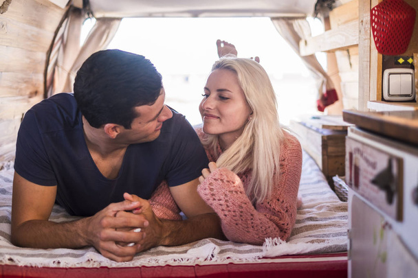 schöne junge Paar sehen einander mit Liebe legen sich in einem alten Oldtimer-Van wie zu Hause. winziges Haus für Liebhaber im Urlaub für alternatives Tagesleben wie Hippie-Modern. - Foto, Bild
