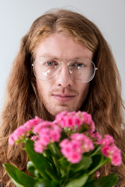 portrait of stylish man with curly hair with bouquet of pink flowers looking at camera - Photo, Image
