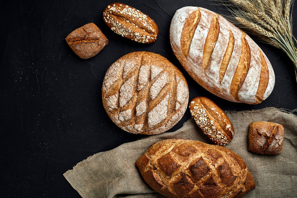Bäckerei - goldene, rustikale, krustige Brotlaibe und Semmeln auf schwarzem Tafelgrund. - Foto, Bild
