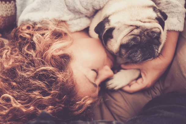 a woman with long curly hair sleeping in a woolen blanket with two pug dog - Photo, Image