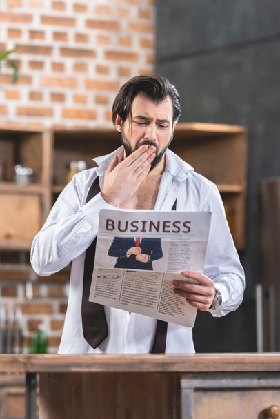 handsome loner businessman reading newspaper and yawning at kitchen - Fotó, kép