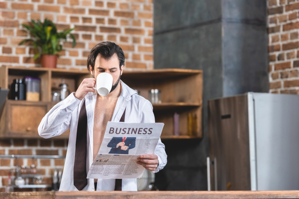 knappe eenling zakenman drinken koffie en het lezen van de krant op keuken - Foto, afbeelding