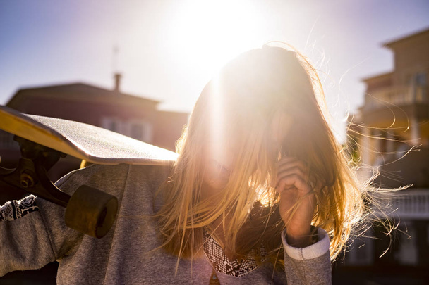 stupenda bella ragazza bionda in controluce ritratto soleggiato con il suo skateboard e vento tra i capelli. vita e libertà concetto di indipendenza
. - Foto, immagini
