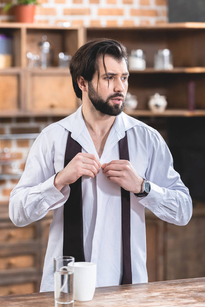 portrait of handsome loner businessman buttoning shirt at kitchen - Фото, изображение