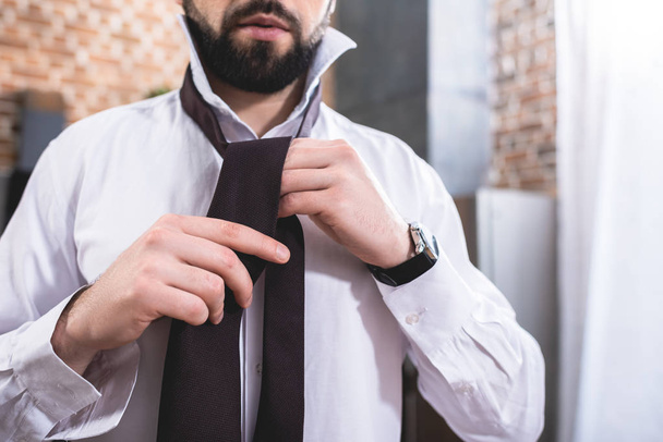 cropped image of loner businessman tying necktie at kitchen - Photo, image