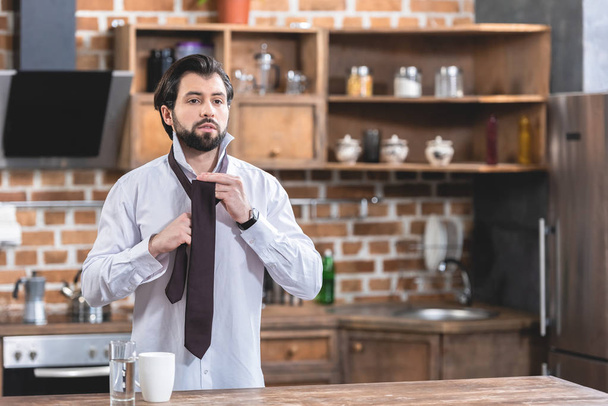 handsome loner businessman tying necktie at kitchen - Zdjęcie, obraz