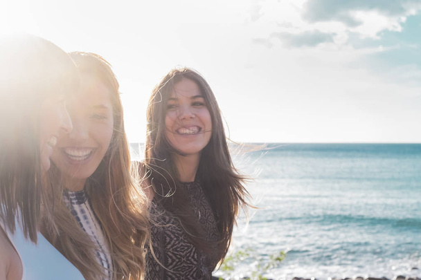3 nuorta naista kävelee rannalla katsellen toisiaan, nauraen ja viettäen vapaa-aikaa yhdessä. kauniina kesäpäivänä. aurinko ja meri taustana
. - Valokuva, kuva