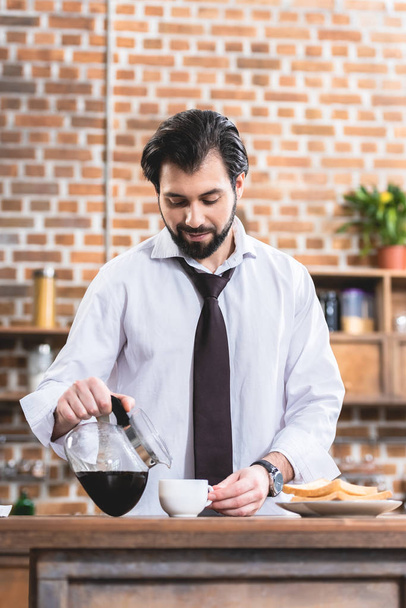 όμορφος μοναχικός επιχειρηματίας ρίχνει καφέ στο φλυτζάνι στην κουζίνα - Φωτογραφία, εικόνα