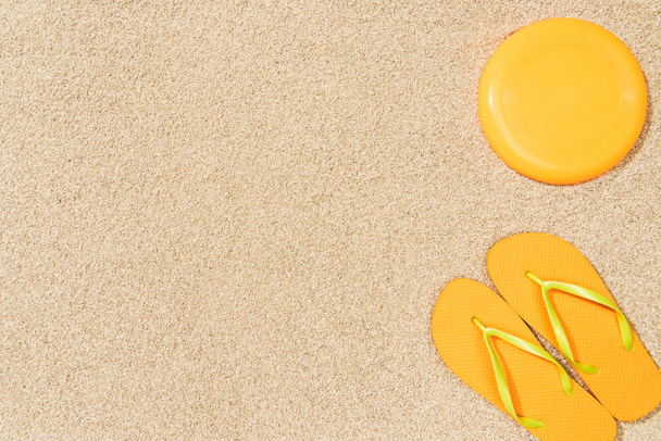top view of yellow flip flops and frisbee on sand - Foto, Imagen