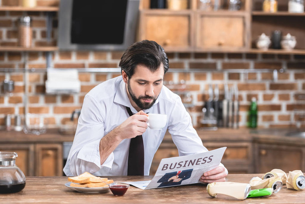 handsome loner businessman drinking coffee and reading newspaper in morning at kitchen - Фото, изображение