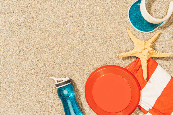 flat lay with water bottle, towel, cap, frisbee and sea star on sand - Foto, immagini