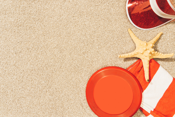 flat lay with red cap, flying disk, towel and sea star on sand - Фото, зображення