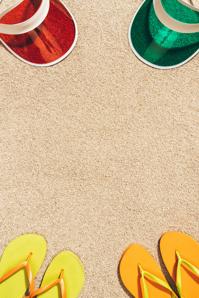 top view of arranged colorful caps and flip flops on sand - Фото, изображение