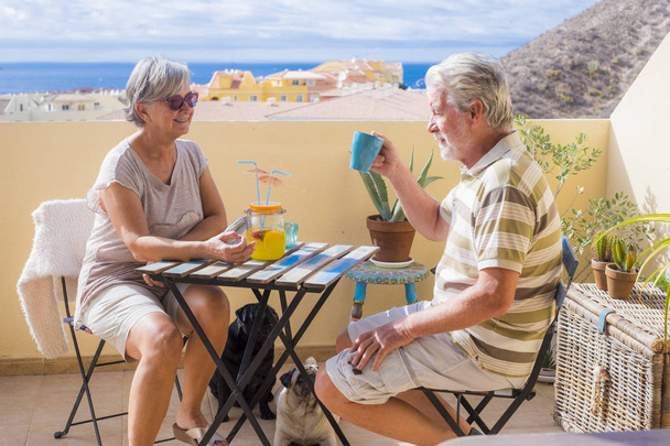 美しい海の景色を望む屋上テラスでシニア高齢者ドリンク フルーツ ジュースのカップル。休暇と退職のコンセプト - 写真・画像