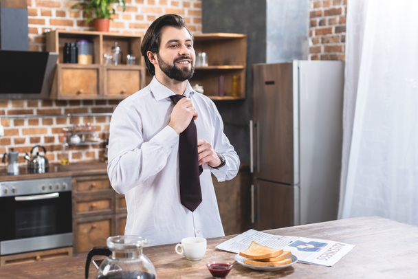 handsome loner businessman fixing tie at kitchen - Zdjęcie, obraz