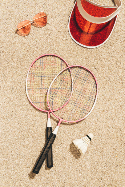 bovenaanzicht van badminton apparatuur, zonnebril en GLB op zand - Foto, afbeelding