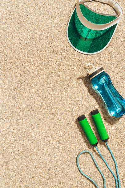 top view of arranged cap, water bottle and jump rope on sand - Foto, Bild