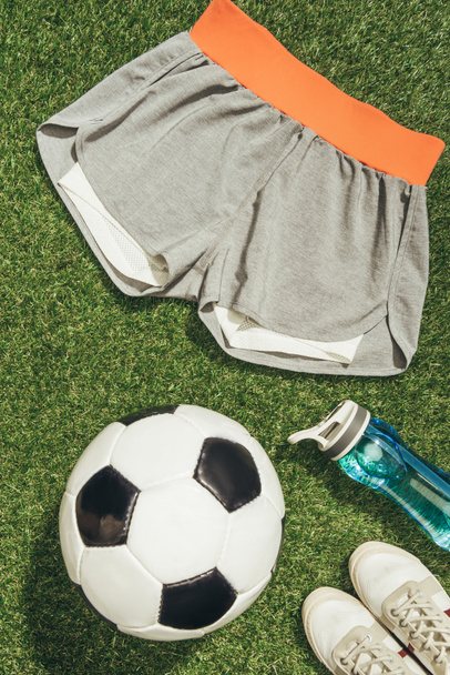 Układ płaski z piłki nożnej, Odzież sportowa, butelkę wody i trampki na zielonej trawie - Zdjęcie, obraz
