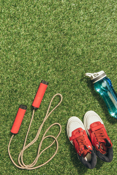top view of arranged water bottle, skipping rope and sneakers on green grass - Foto, Imagem