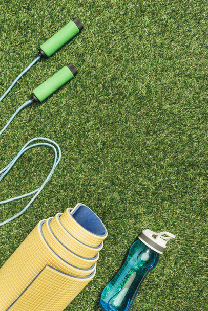 top view of arranged yellow mat, skipping rope and water bottle on green grass - Fotografie, Obrázek