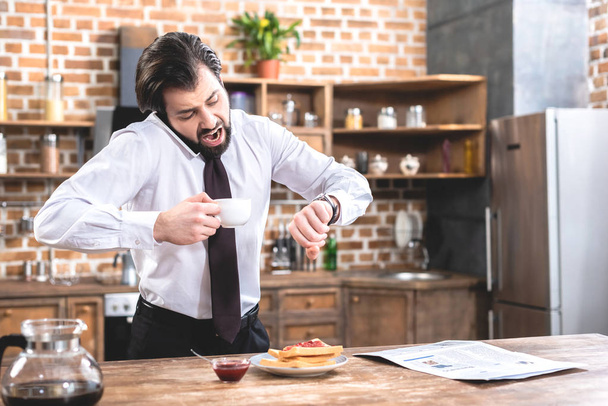 shocked handsome loner businessman talking by smartphone and checking time at kitchen - Photo, Image