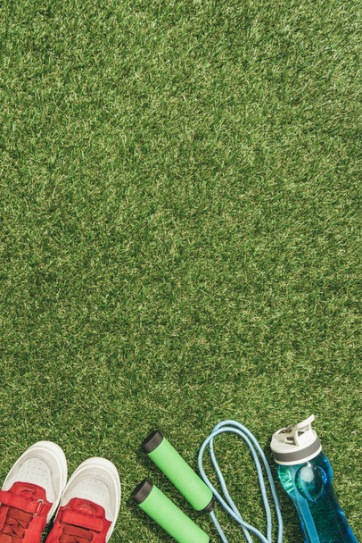 top view of arranged water bottle, jump rope and sneakers on green grass - Foto, Imagem