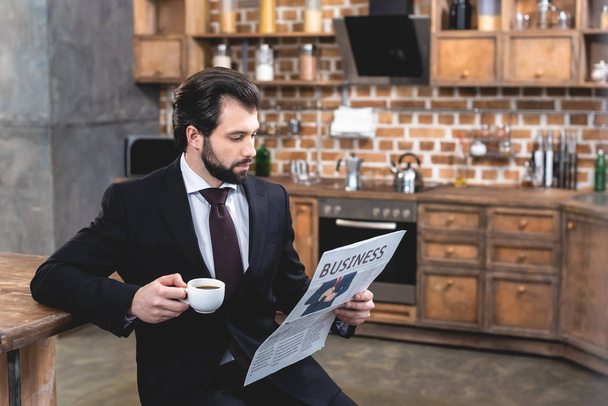 samotnik przystojny biznesmen czytanie gazety i trzymając kubek kawy rano w kuchni - Zdjęcie, obraz