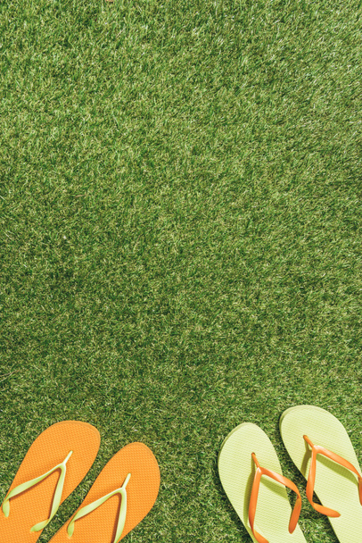 top view of green and orange flip flops on green lawn - Foto, Imagen