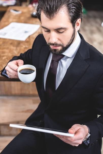 vue grand angle de bel homme d'affaires solitaire regardant tablette et tenant une tasse de café à la cuisine
 - Photo, image