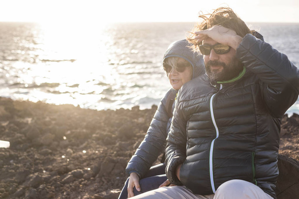 Matka i syn spędzić czas razem siedzący na skale uśmiechając się i patrząc na morze i góry - Zdjęcie, obraz