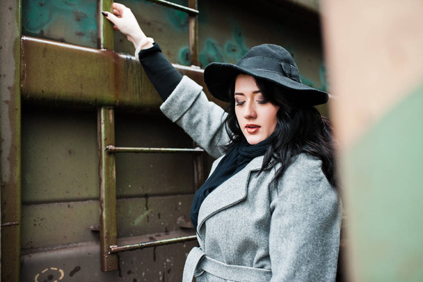 Μελαχρινή κοπέλα σε γκρι παλτό με καπέλο σε σιδηροδρομικό σταθμό. - Φωτογραφία, εικόνα