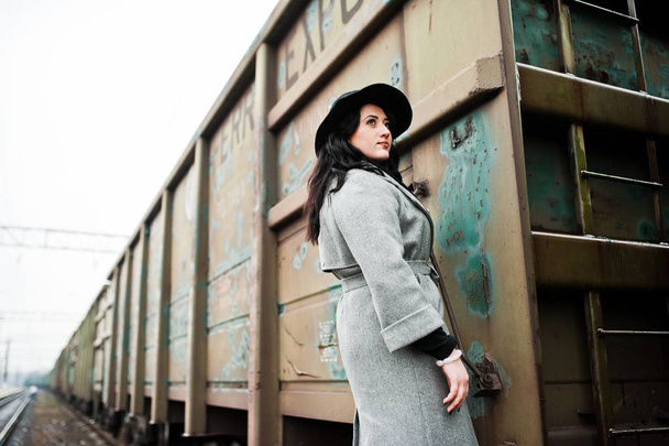 Brunette girl in gray coat with hat in railway station. - Photo, image