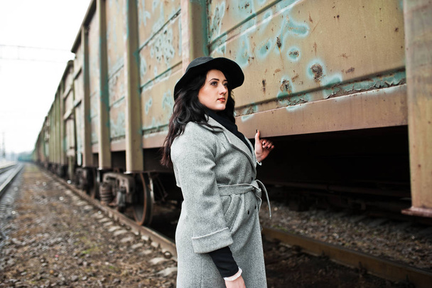 Brunette girl in gray coat with hat in railway station. - Фото, изображение