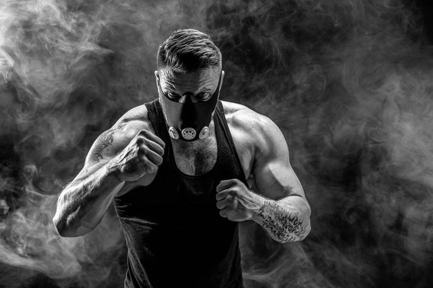 Strong male athlete in a black training mask on a black background - Foto, immagini