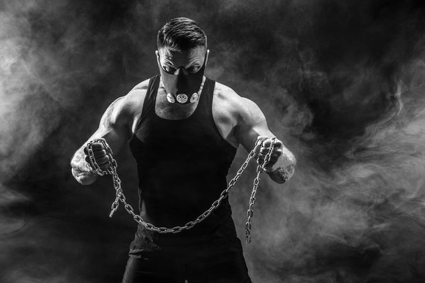 Portrait of muscular sportsman tearing metal chain. Black background with smoke - Foto, immagini